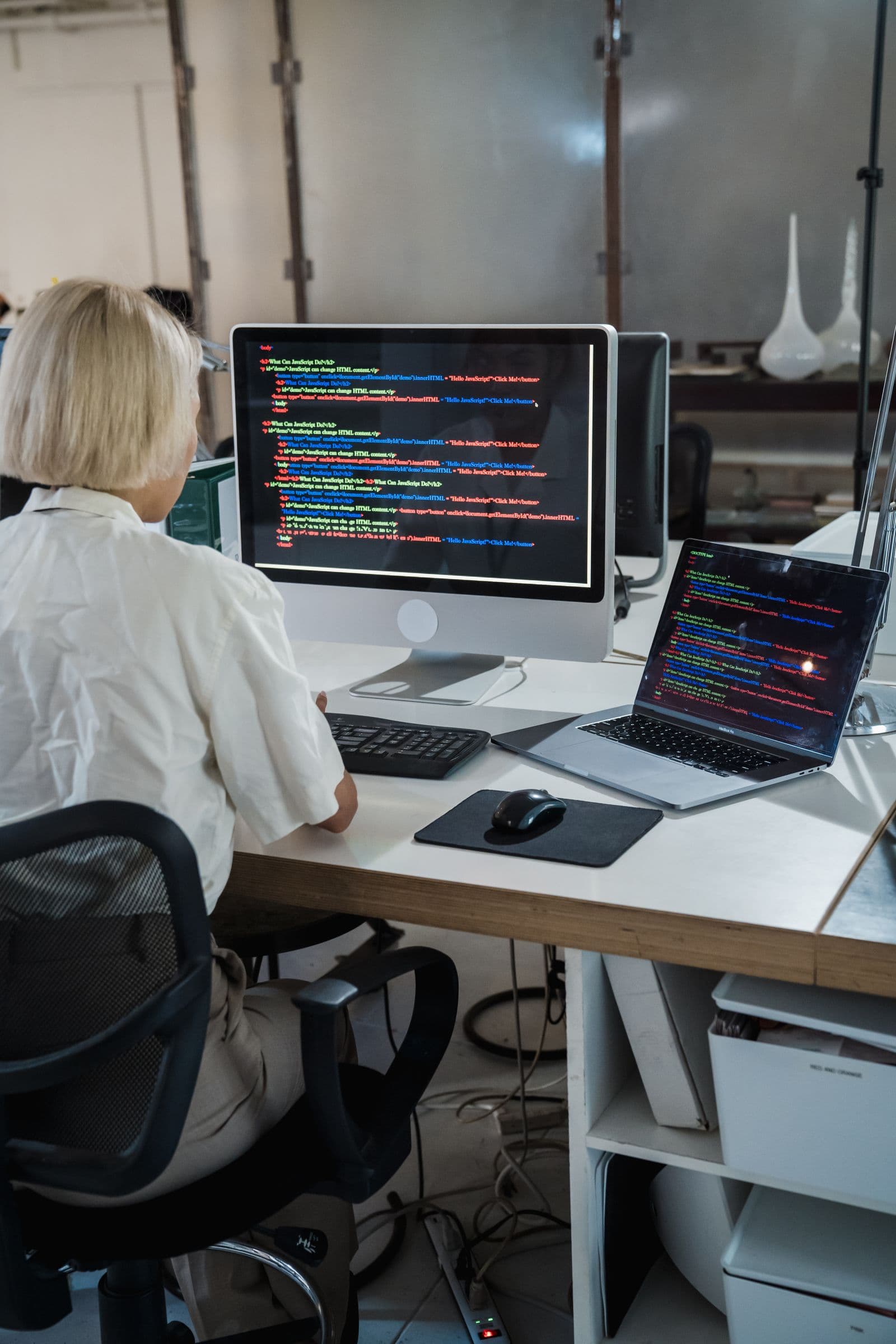 Une développeuse devant deux écrans de code dans un bureau